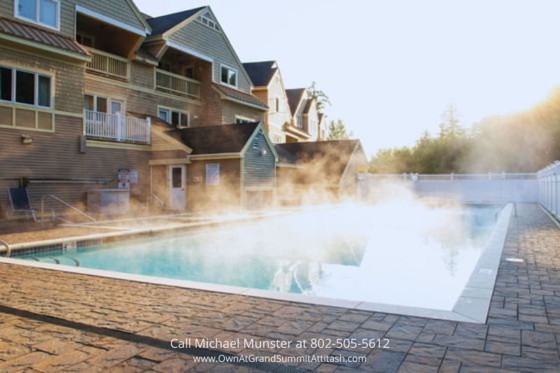 Heated outdoor pool at the Grand Summit Hotel emitting steam in the cool morning air, offering a luxurious and relaxing swimming experience for guests, with the hotel building as a charming backdrop.