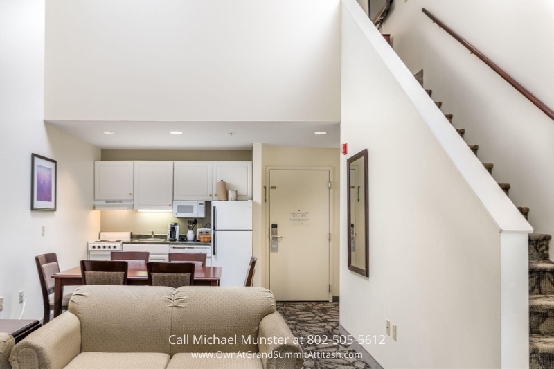 Bright and spacious living room area in a suite at the Grand Summit Hotel, featuring comfortable sofas, a dining area, and an open-plan design, perfect for relaxing and socializing in style.