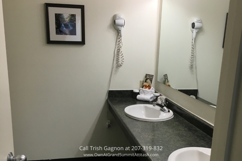 Modern bathroom in a unit at the Grand Summit Hotel, featuring a single sink with a black countertop, a wall-mounted hairdryer, and a large mirror. The space is well-lit with bright lighting, and a framed picture decorates the wall, adding a touch of elegance.