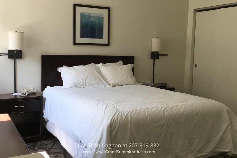 Cozy bedroom in a unit at the Grand Summit Hotel, furnished with a comfortable queen-sized bed with white linens, bedside tables, and modern wall-mounted lamps. A piece of framed artwork hangs above the headboard, creating a welcoming and relaxing atmosphere.