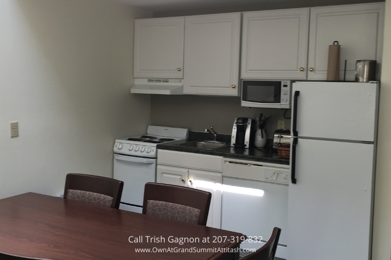 Fully-equipped kitchen in a unit at the Grand Summit Hotel, featuring white cabinetry, a full-sized refrigerator, an electric stove, microwave, and a dishwasher. The kitchen has all the essentials for a comfortable stay, with ample counter space and a dining table with chairs nearby.