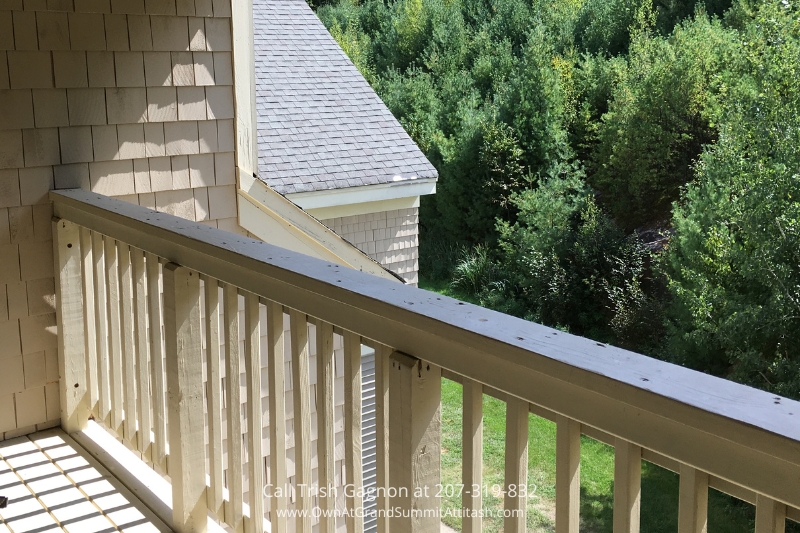 Private covered deck in a unit at the Grand Summit Hotel, providing a serene view of the surrounding greenery. The deck features wooden railings and offers a peaceful outdoor space for guests to enjoy the natural beauty of the area.