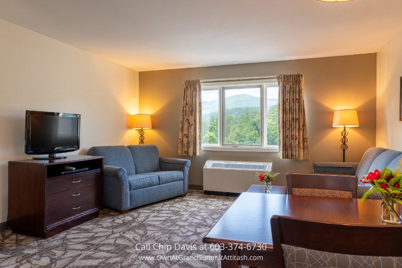 A bright and inviting living space in a Grand Summit Hotel unit, featuring a comfortable seating area, a dining table, and a large window with picturesque mountain views.