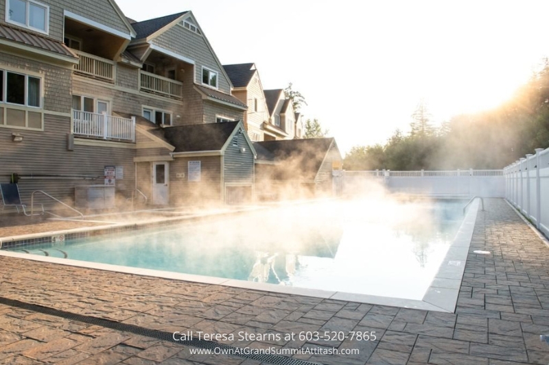 Steam rises from the heated outdoor pool at the Grand Summit Hotel, creating a serene ambiance with the backdrop of the resort's classic architecture and surrounding forest.