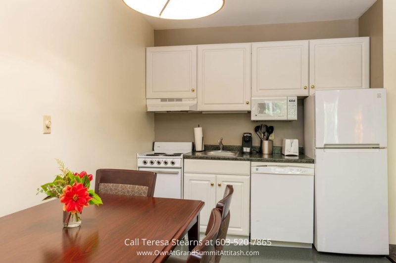 Functional kitchen and dining area in a Grand Summit Hotel unit, with white cabinetry, modern appliances, and a polished wooden dining table adorned with a fresh floral centerpiece.