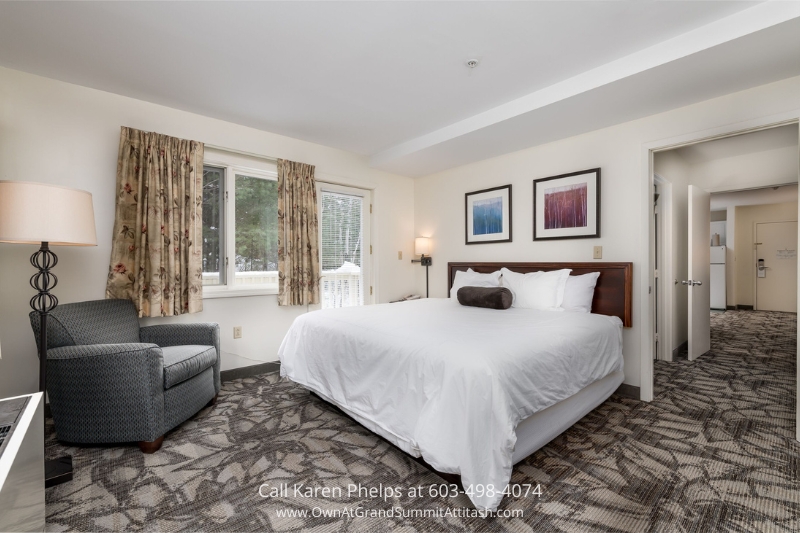 Spacious bedroom in Unit 149 Interval 3 featuring a large white bed, cozy armchair, and mountain views through double windows
